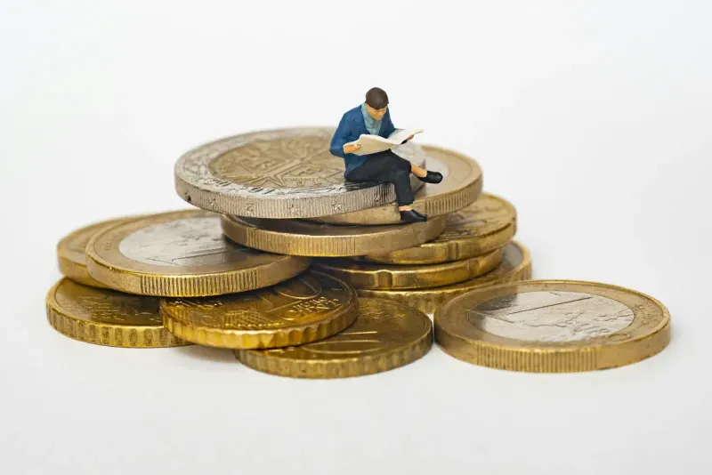 Miniature figure sitting on a stack of coins reading a newspaper
